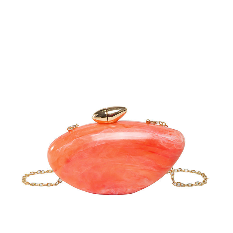 Oval shell acrylic evening bag in coral color with a gold clasp and chain strap.