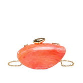 Oval shell acrylic evening bag in coral color with a gold clasp and chain strap.