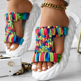 Braided summer sandals featuring a vibrant rainbow stripe pattern and thick white sole for comfort and style.